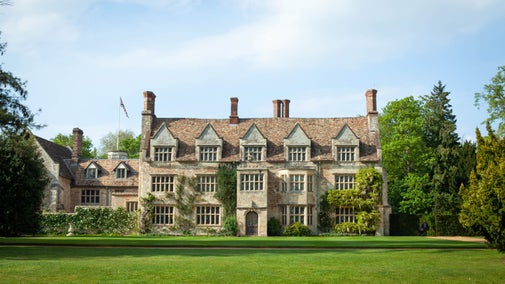 An early summer photo showing a stone Jacobean house with blue sky and green trees